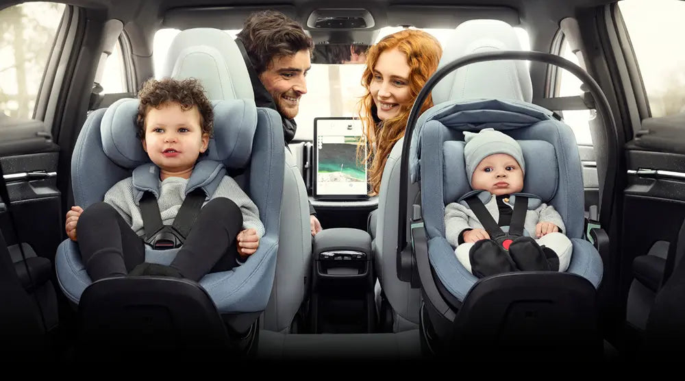 Blick durch die Heckscheibe auf eine Familie im Auto: Ein Kleinkind im Thule Elm Reboarder-Kindersitz und ein Baby in der Thule Maple Babyschale fahren sicher rückwärtsgerichtet.