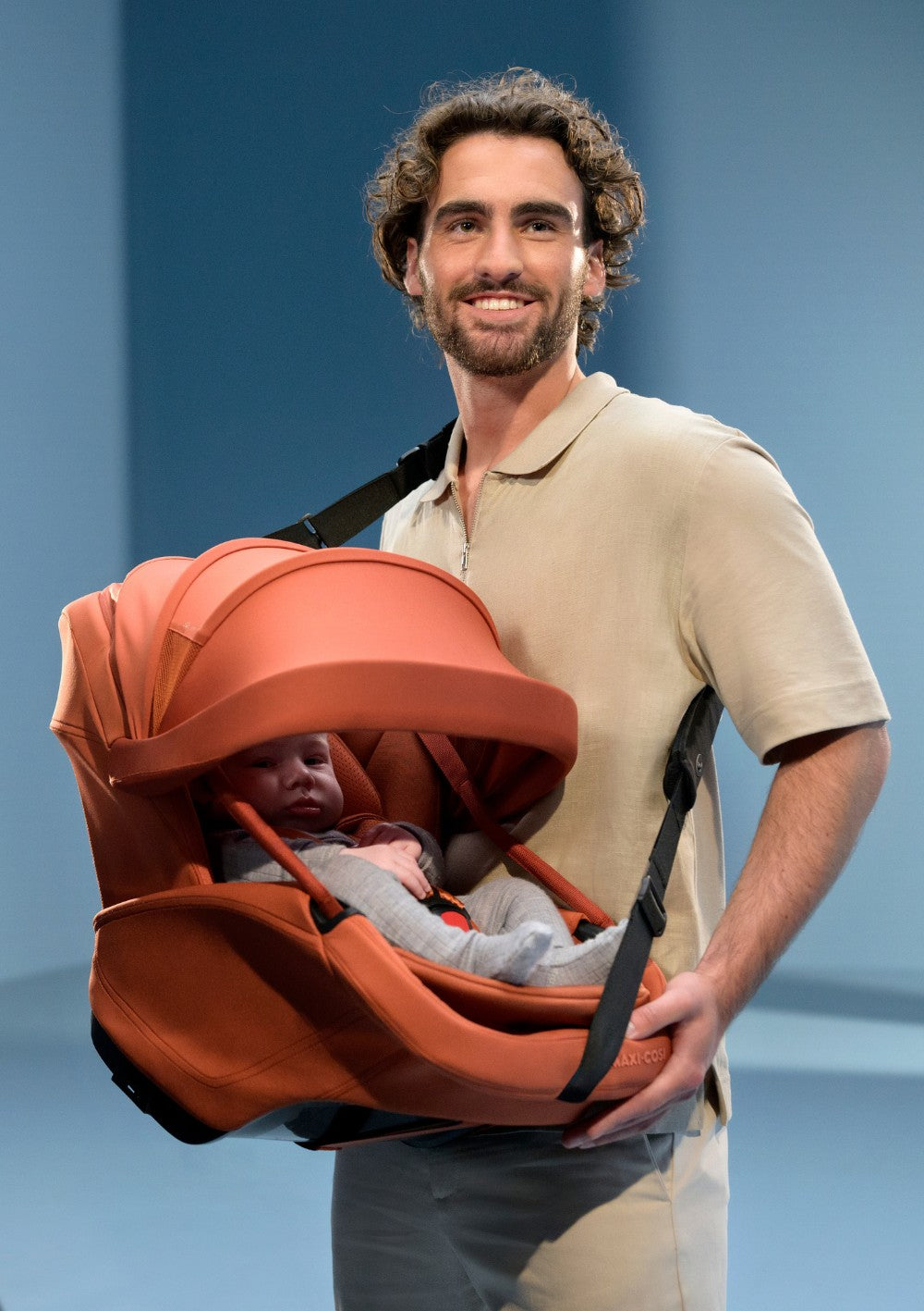 Mann trägt Maxi-Cosi Babyschale 'Coral Slide Pro' Copper Terra mit Tragegurt