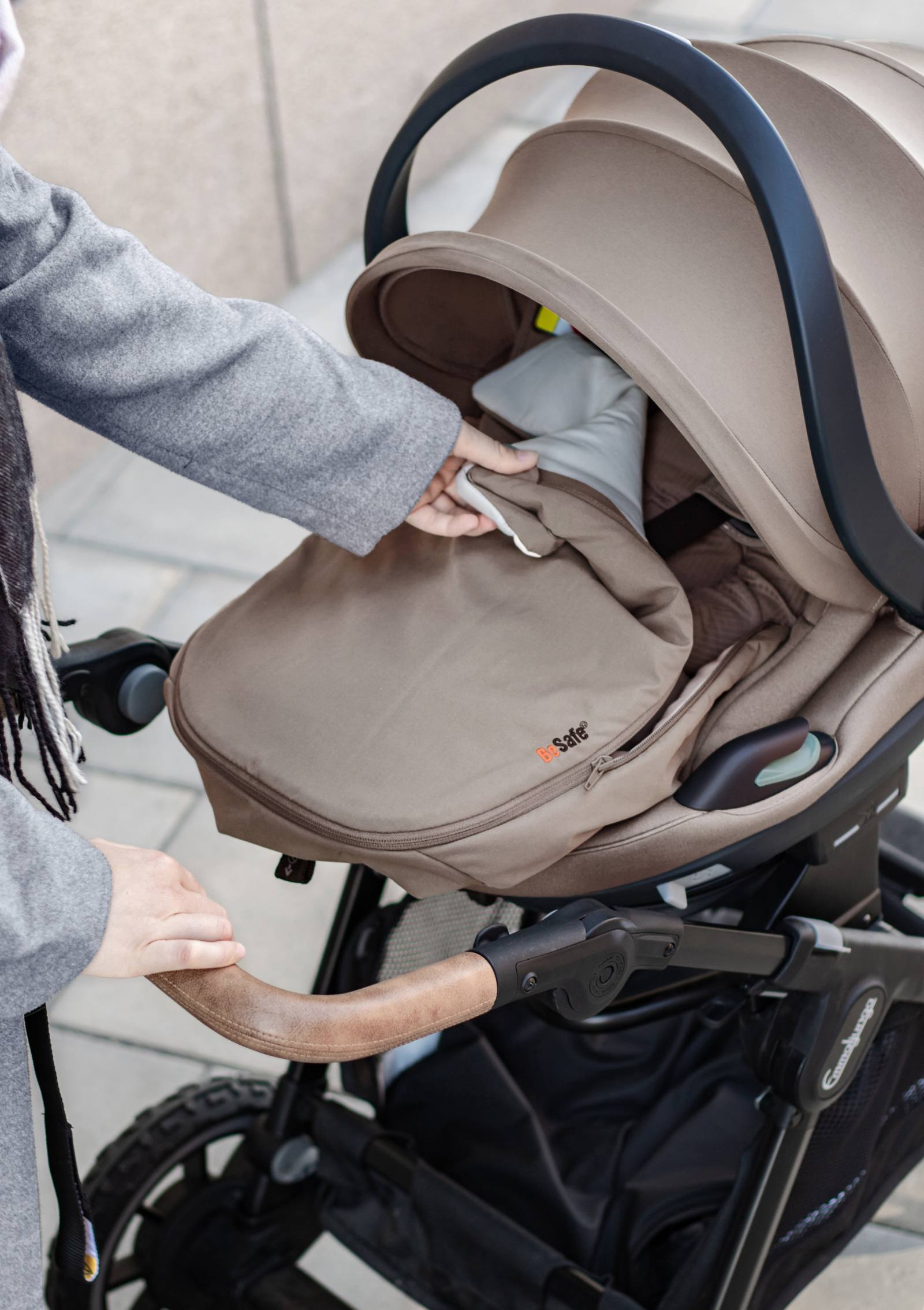 Frau öffnet BeSafe Wind & Weather Cover für Babyschale 'Go Beyond' Dark Sand