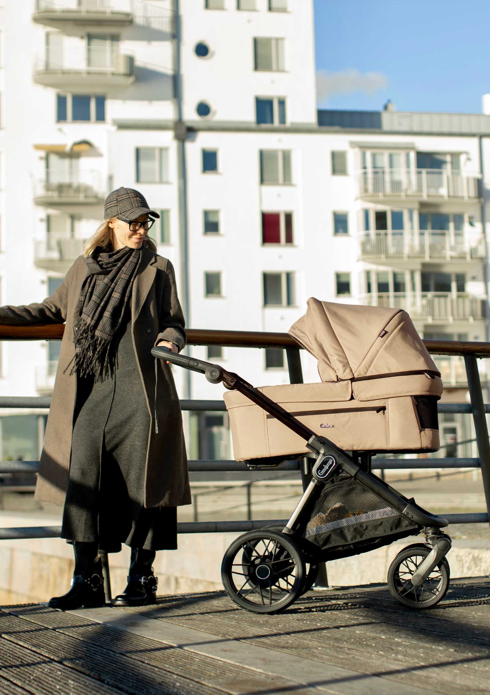 Frau mit Emmaljunga Kinderwagen-Set 'SENTO PRO' Urban Dune steht an Gelände angelehnt