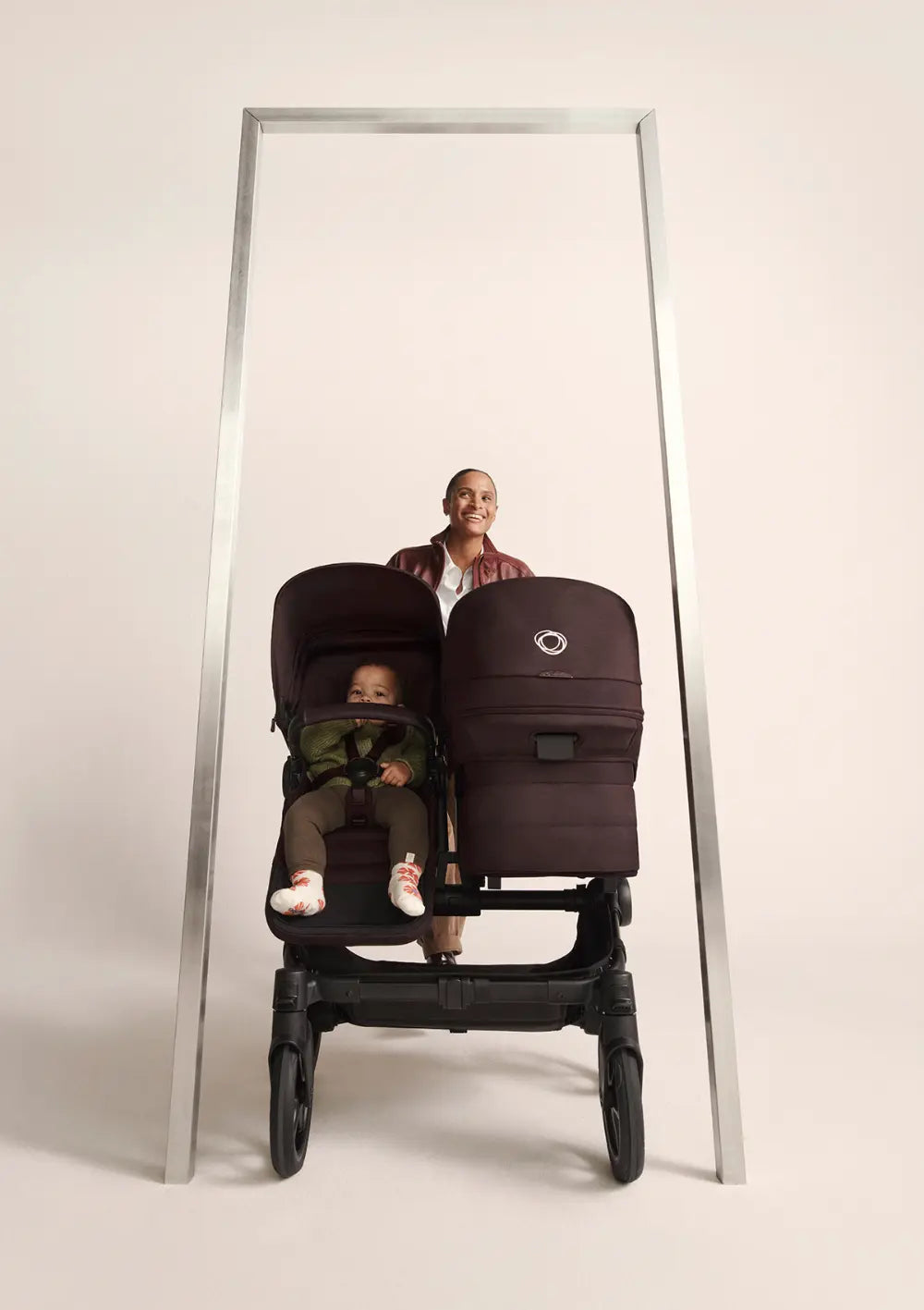 Frau schiebt Bugaboo Geschwisterwagen 'Donkey 6 Duo' Cocoa Brown durch ein Türrahmengestell