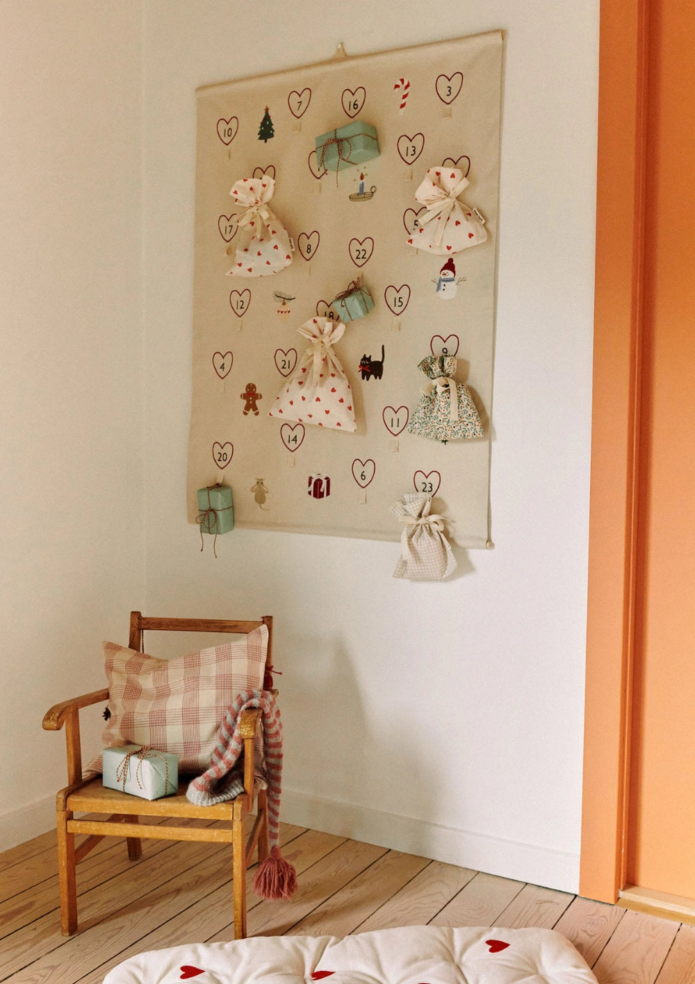 Der beigefarbene Stoff-Wandkalender Dear April Adventskalender Halo Holiday Mix hängt voll bestückt mit kleinen Päckchen und Stoffbeuteln an einer weißen Wand im Kinderzimmer.