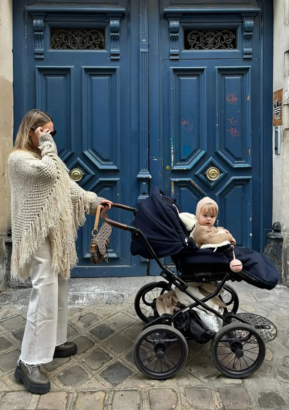 Mutter steht mit dem Angelcab Kinderwagen-Set 'C3-Series' Pacific vor einer blauen Altbautür in der Stadt