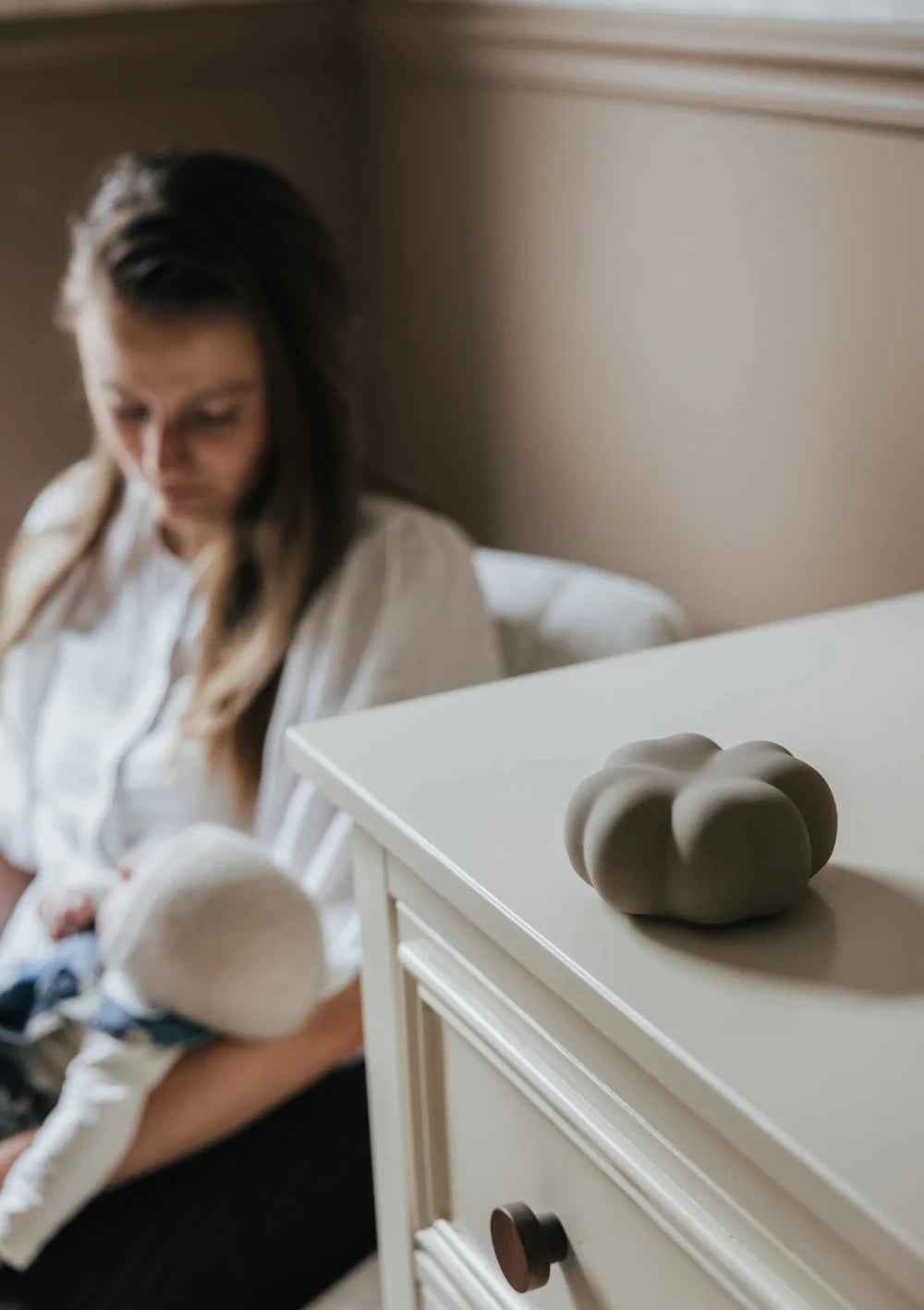 flow AMSTERDAM Nachtlicht Kleeblatt 'Luck' soft clay leigt auf einer Kommode, dahinter sitzt eine Mutter mit Baby