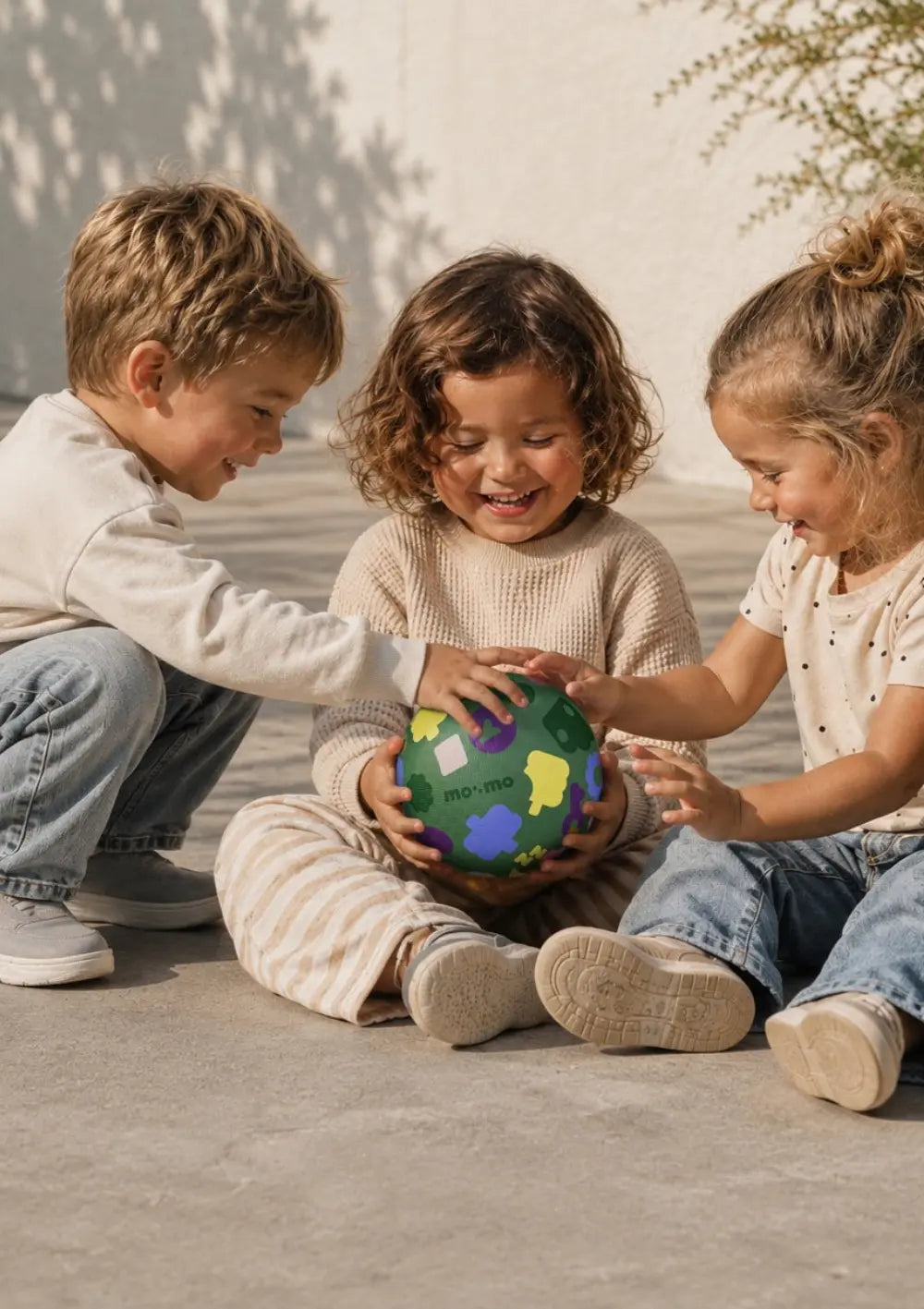 Drei lachende Kinder beim Spielen mit dem grünen Ball aus dem mo:mo Starter-Set 'Bouncing Buddy' Spielball mit App-Zugang Spinach