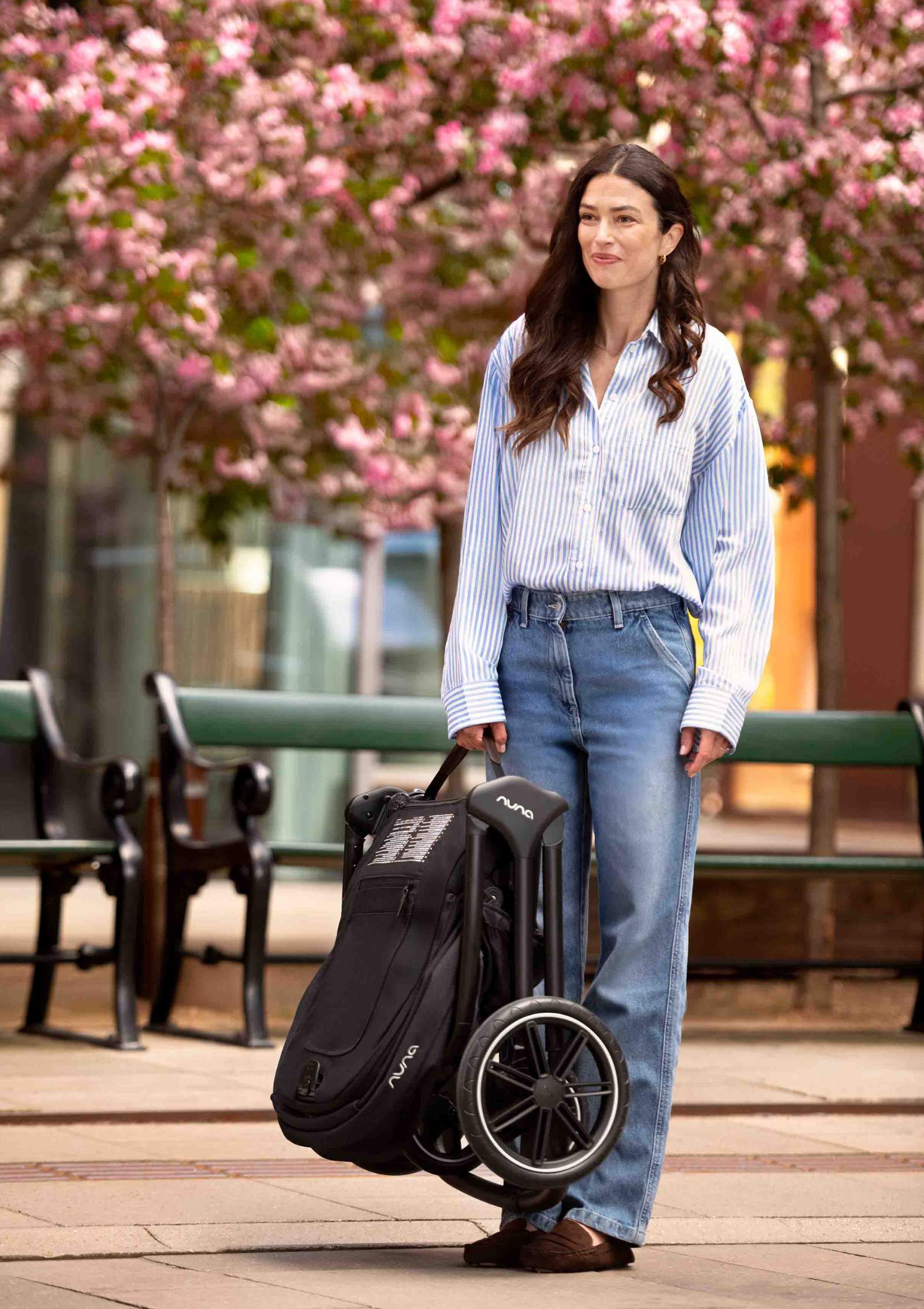 Frau trägt Nuna Kinderwagen TRIV lx Caviar kompakt zusammengeklappt