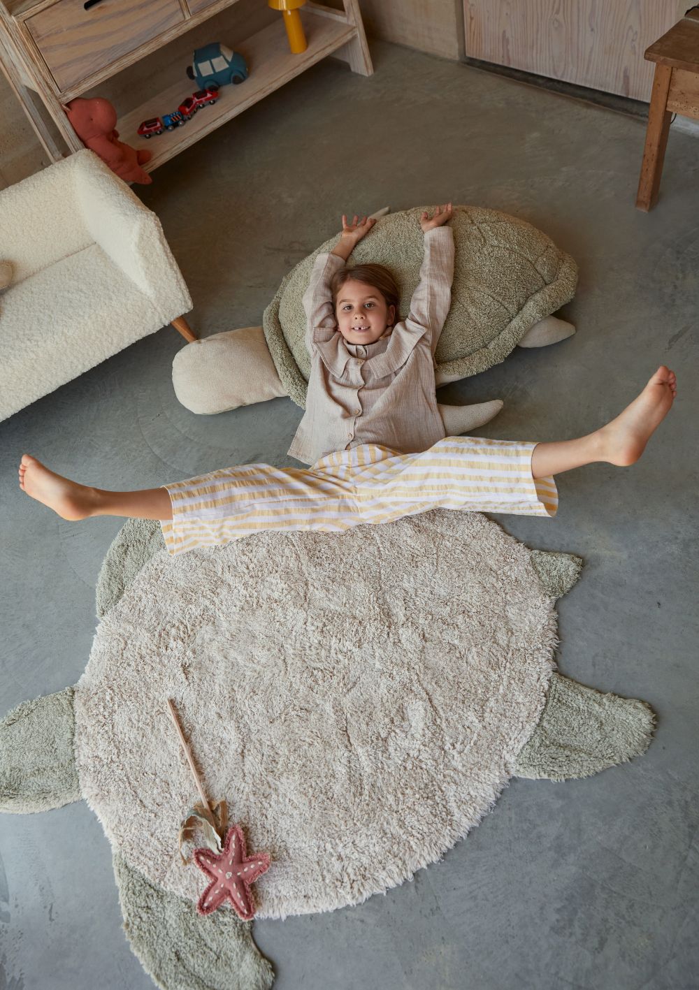 Lorena Canals Teppich mit Tiermotiv 'Sea Turtle' 130 x 110 cm – Kind liegt auf Teppich und passendem Stofftier