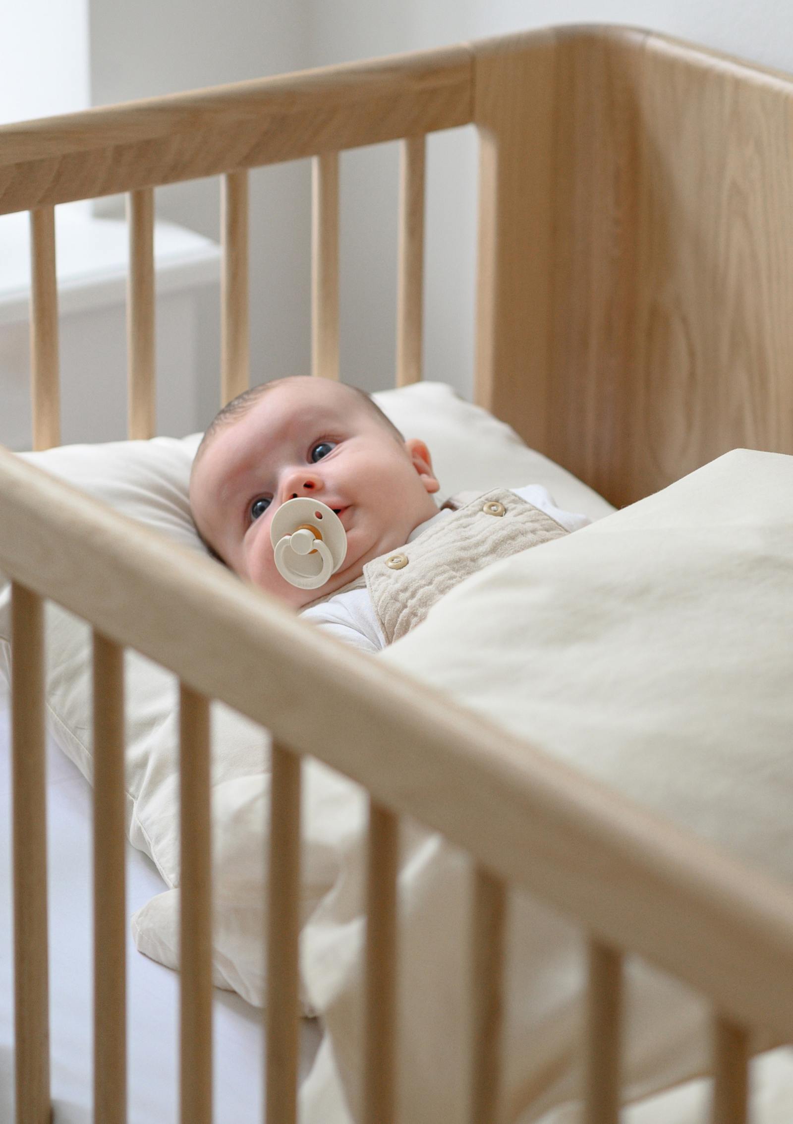 Baby liegt im We Are Bitte Babybett 'Nature Baby Bed 2.0' Eiche 124,5 x 72,5 cm