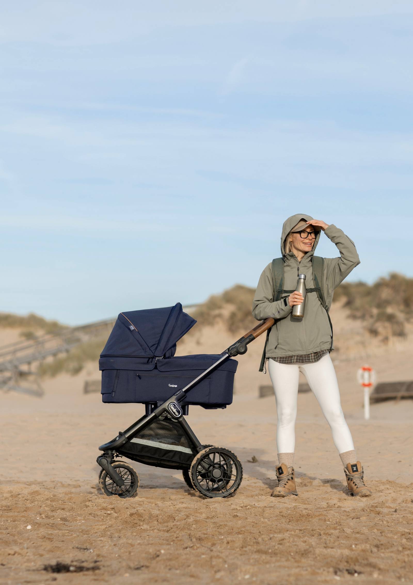 Frau in sandiger Dünenlandschaft unterwegs mit Emmaljunga Kinderwagen 'SENTO PRO' Outdoor Dark Navy