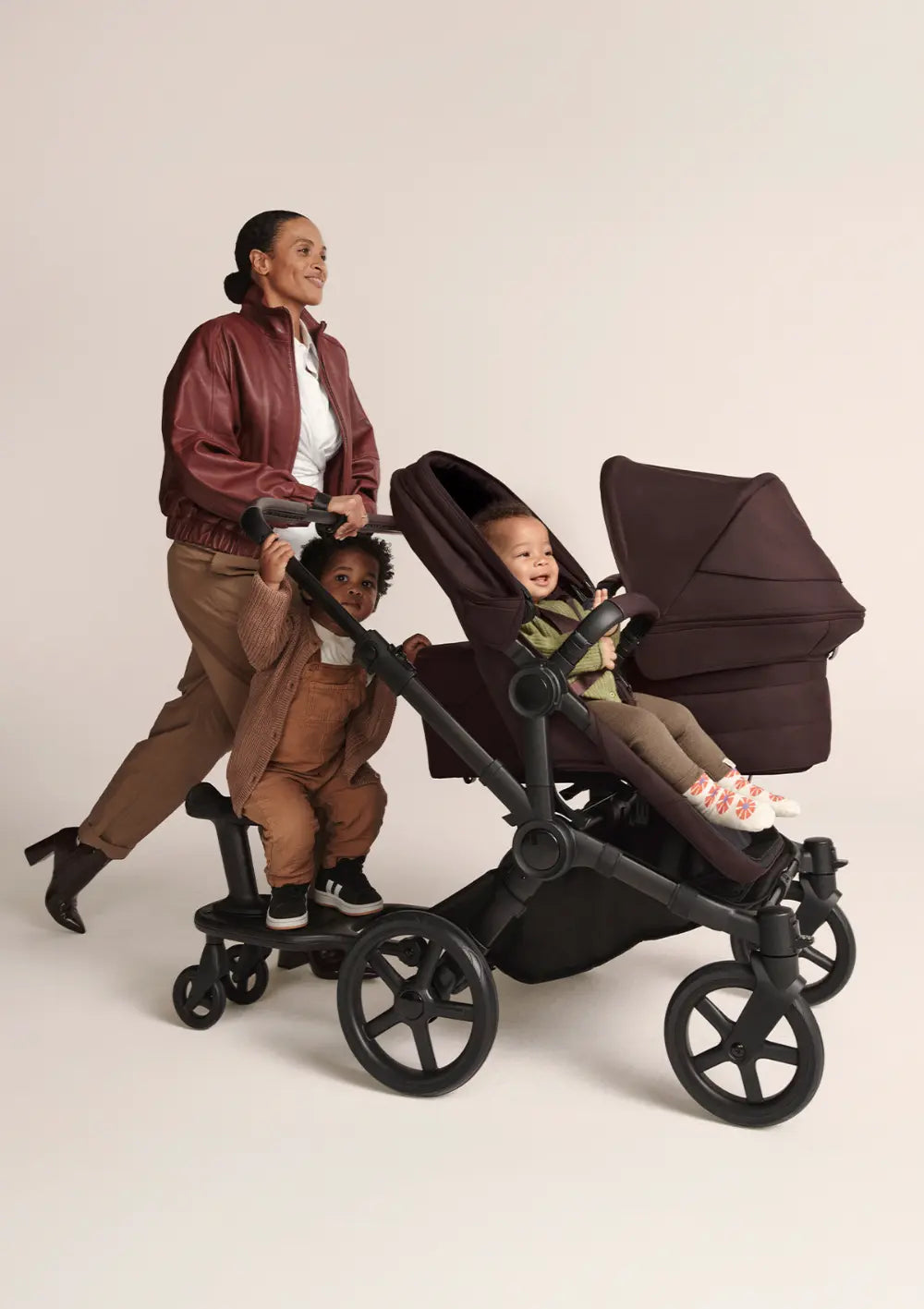 Frau schiebt mehrere Kinder im Bugaboo Geschwisterwagen 'Donkey 6 Duo' Cocoa Brown mit Babywanne, Sportsitz und Mitfahrbett