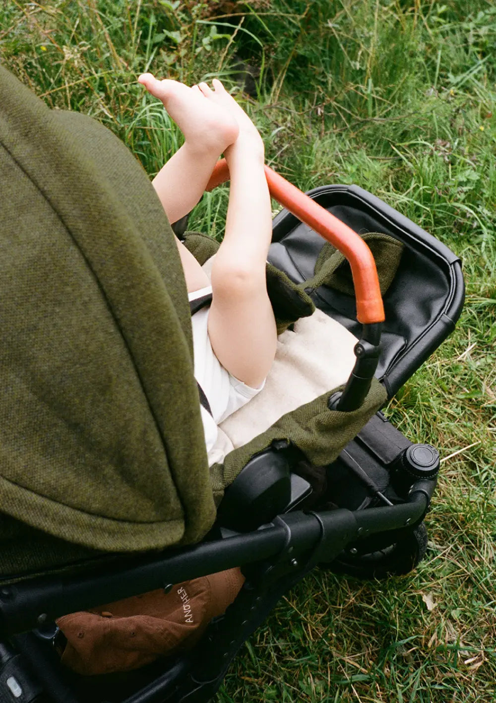 Kind sitzt im Sportsitz des Angelcab Kinderwagens 'U3-Series' Kentish und streckt die Beine in die Luft, im Hintergrund ist eine Wiese zu sehen