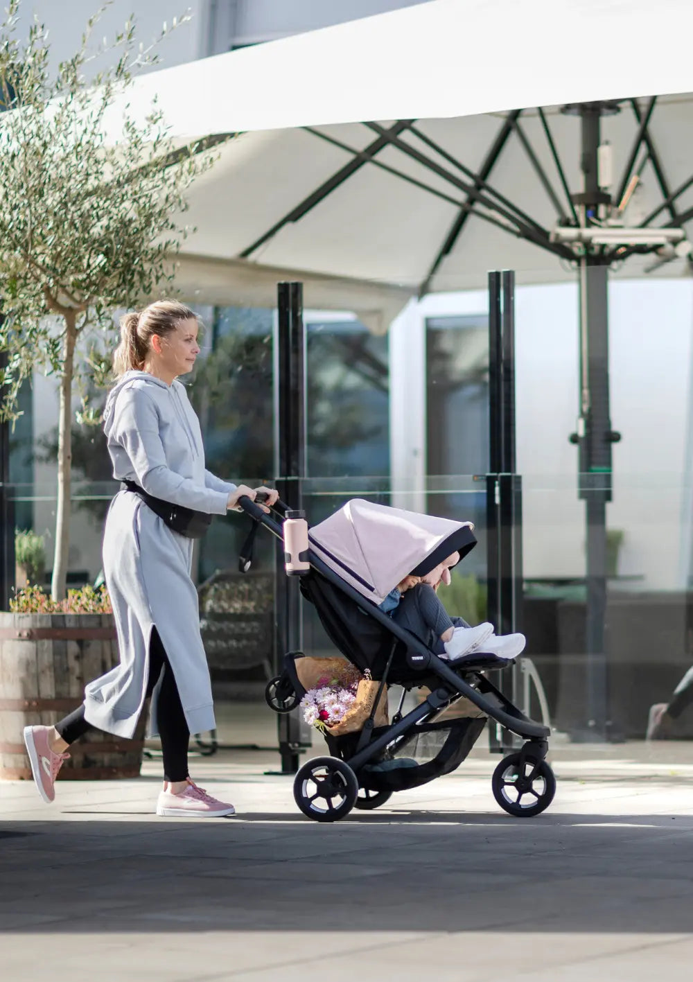 Frau schiebt den Kinderwagen mit hochgeklapptem Thule Mitfahrbrett 'Rider Board